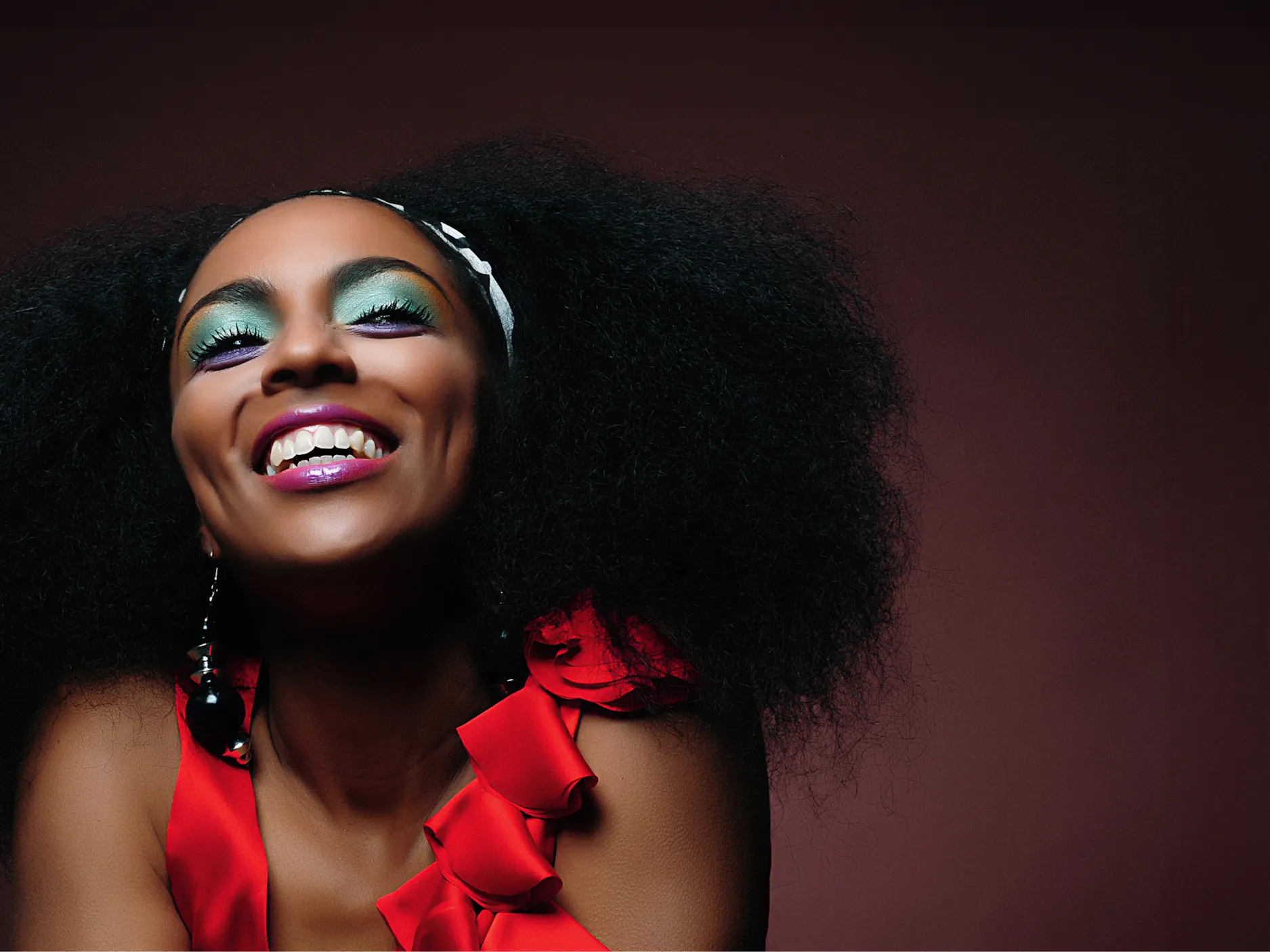 Portret nasmejane intervjuvanke od prsi navzgor, na sebi ima barvita ličila in živo rdečo majico